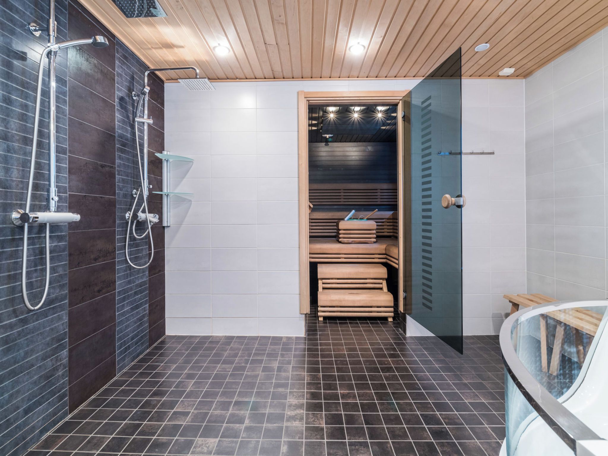 A modern bathroom with a shower, a glass-enclosed sauna, and a wooden bench.