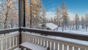 Un balcón de madera con un banco, con vista a un bosque nevado bajo un cielo despejado.