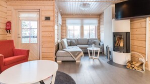Un interior de cabaña acogedor con un sofá, un sillón rojo, una mesa redonda y una chimenea.