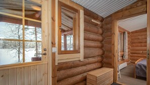 Het interieur van een blokhut met een houten bank, een kleine tafel en een raam met uitzicht op een besneeerd landschap.