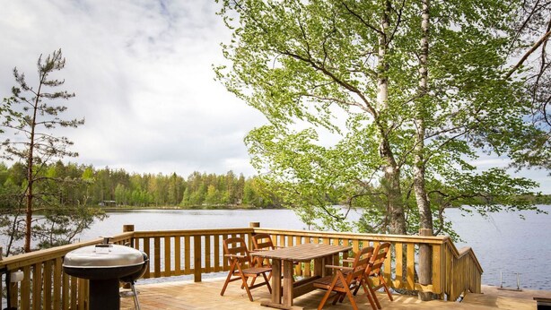 Een houten terras met een barbecue, stoelen en een tafel, met uitzicht op een meer.