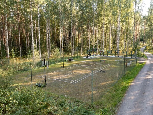 A basketball court surrounded by a forest with tall trees.
