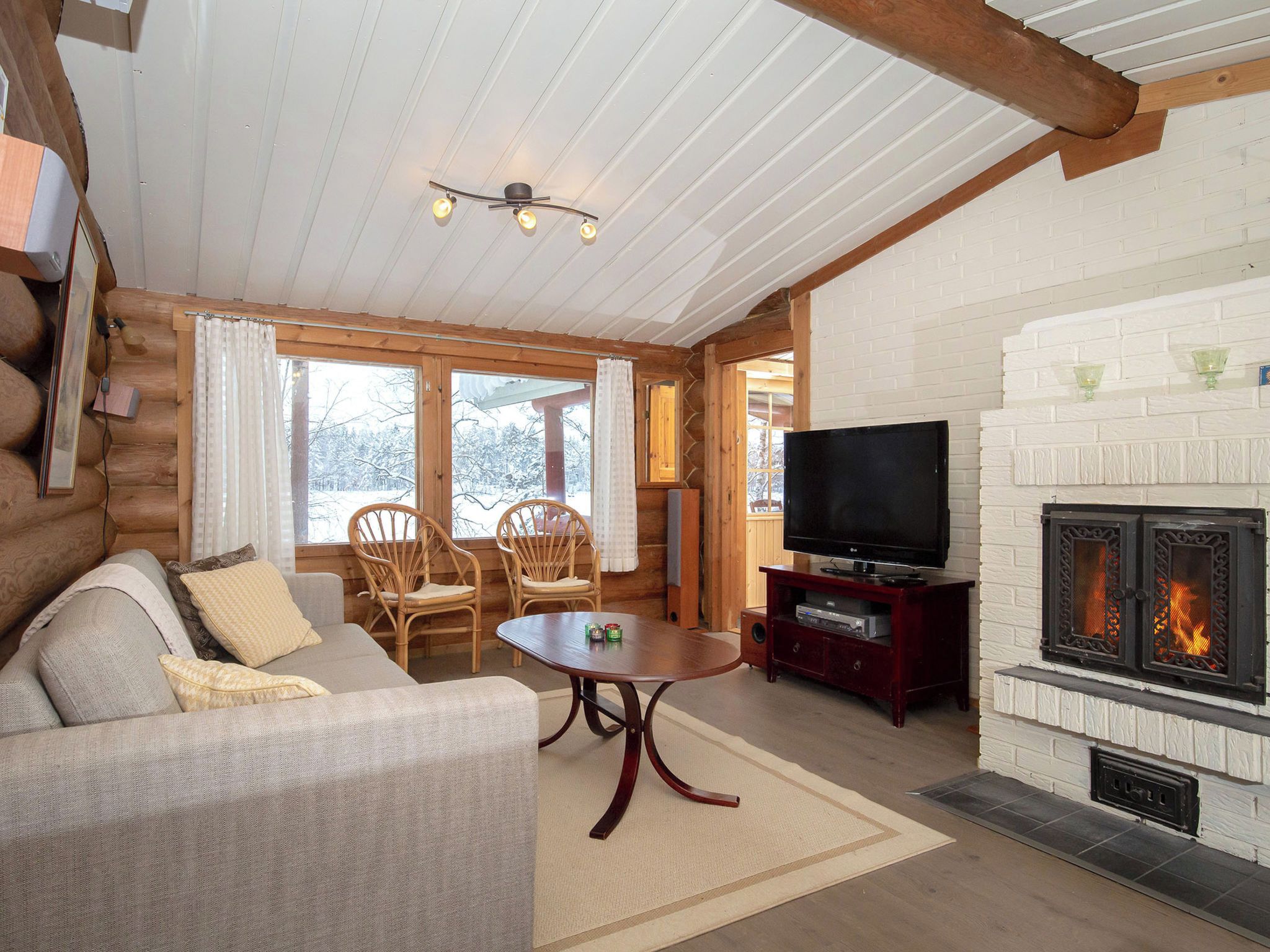 L’intérieur d’un chalet confortable, avec des murs en bois, un canapé, des fauteuils, un téléviseur et une cheminée.