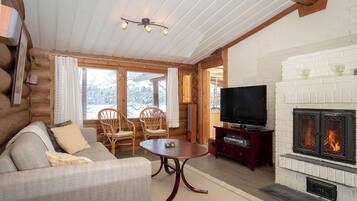 L’intérieur d’un chalet confortable, avec des murs en bois, un canapé, des fauteuils, un téléviseur et une cheminée.