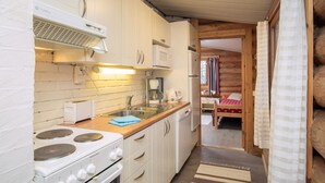 Een kleine keuken met een fornuis, magnetron en spoelbak. In de achtergrond staat een bed.