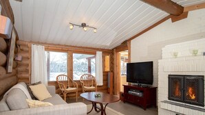 Een gezellig interieur van een houten chalet met een open haard, een bank, een televisie en een eettafel.