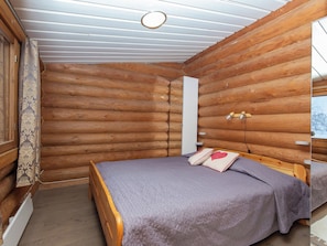 Een slaapkamer in een blokhut met een bed, een raam en een houten plafond.