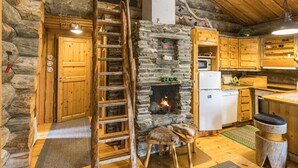 Ein rustikales Blockhaus-Interieur mit Kamin aus Stein, einer Holzleiter und einer Küchenzeile.