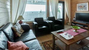 A cozy living room with a leather sofa, two black chairs, a wooden coffee table, a TV, and a large window with curtains. - Ylläksen rinnemäki b by Interhome (Ylläsjärvi)