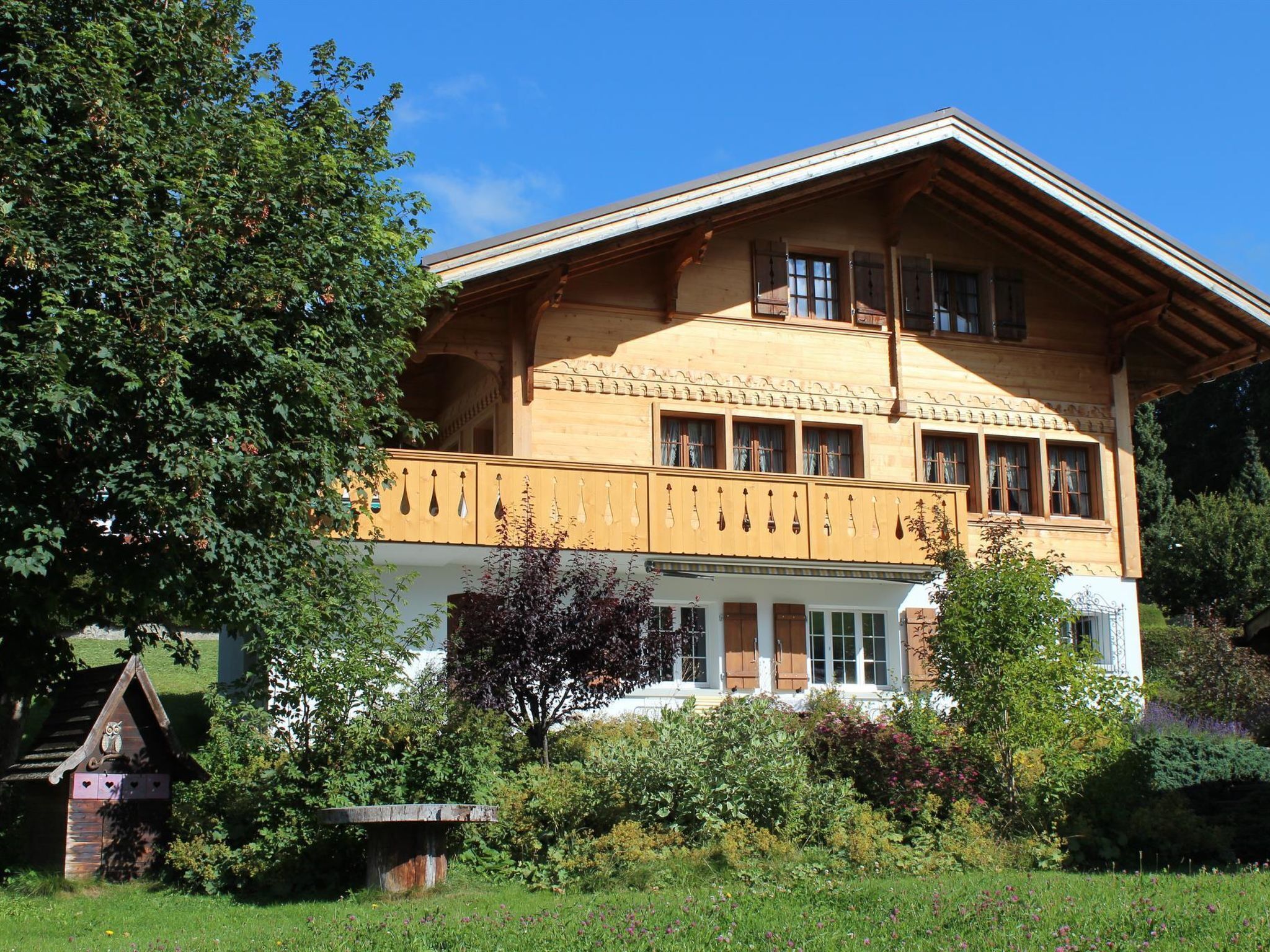 Ein großes, zweistöckiges Holzhaus mit Balkon, umgeben von üppigem Grün und einem gepflegten Garten.