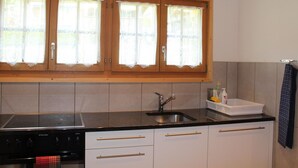 Een keuken met houten kastjes, een zwart aanrecht en een raam met kantgordijnen.