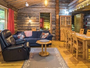 A log cabin interior with a leather sofa, a dining table with chairs, a fireplace, and a wooden cabinet. - Lapinkulta by Interhome (Kuusamo)