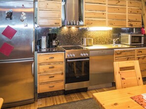 A compact kitchen with a refrigerator, stove, microwave, and wooden cabinets. - Lapinkulta by Interhome (Kuusamo)