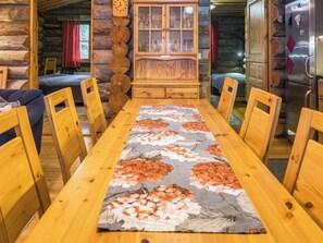 A wooden dining table with chairs, a floral table runner, and a wooden cabinet with glass doors. - Lapinkulta by Interhome (Kuusamo)