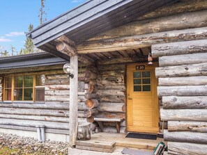 Une cabane en rondins avec une porte en bois portant l’inscription « E 20 », une fenêtre et un porche avec un banc.