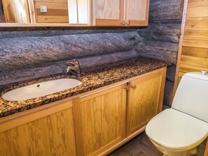 A bathroom with a granite countertop sink, wooden cabinets, and a white toilet.