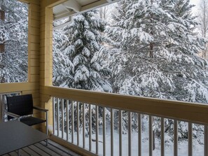 A covered outdoor area with a wooden railing, a table, and chairs, overlooking a snowy landscape with dense evergreen trees. - Vaarapirtti / tähti by Interhome (Sotkamo)