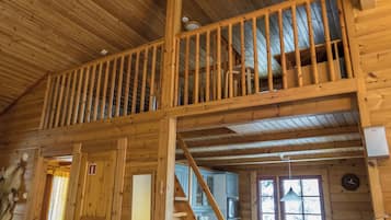 A wooden cabin interior with a loft bedroom, a kitchen area, and a dining space.