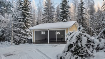 Une maison de plain-pied avec un porche abrité, entourée d’arbres couverts de neige.