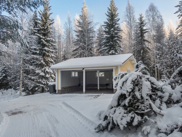 A single-story house with a covered porch, surrounded by snow-covered trees.