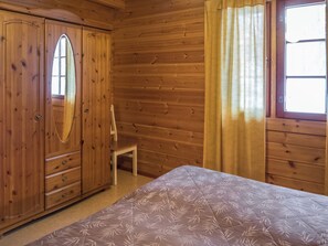 A wooden room with a bed, a wardrobe, and a chair.