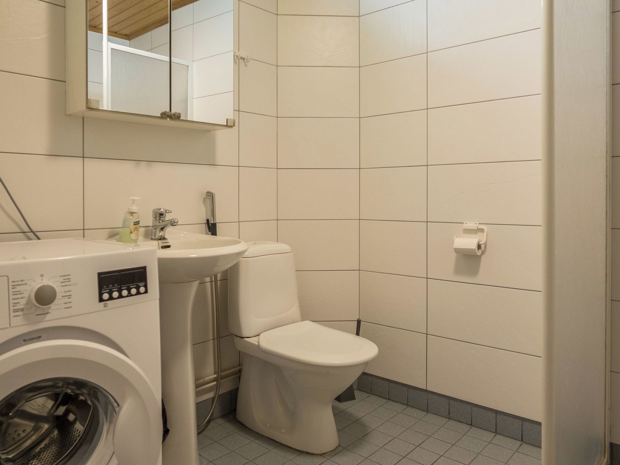 A compact bathroom with a washing machine, a sink, and a toilet.