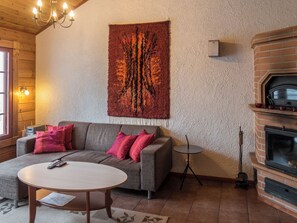 A cozy living room with a sofa, a round table, a fireplace, and a wall tapestry.