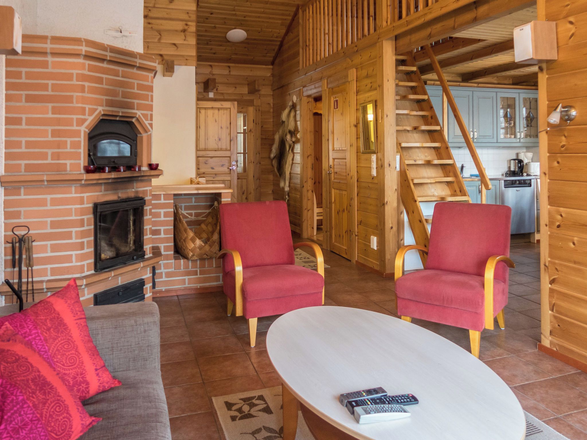 Un salon chaleureux avec une cheminée, deux fauteuils rouges, un canapé et une table basse.
