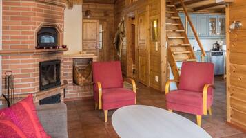 Un salon chaleureux avec une cheminée, deux fauteuils rouges, un canapé et une table basse.