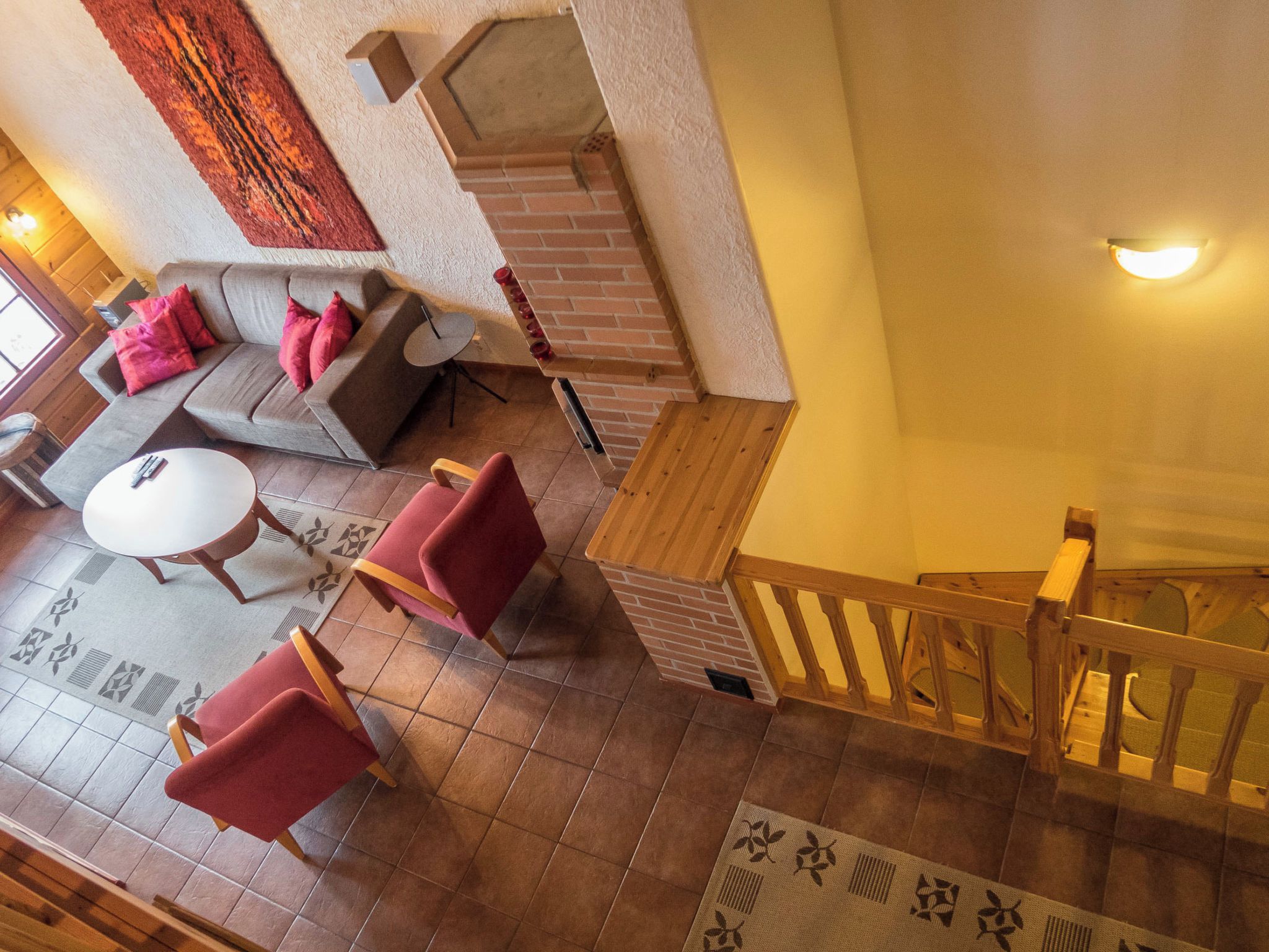 Ein mehrgeschossiges Interieur mit einer Treppe, einer Sofagarnitur, einem runden Tisch und einem gemusterten Teppich.