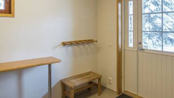 Una habitación con un banco de madera, una mesita, un perchero y una puerta que ofrece vistas a árboles cubiertos de nieve.