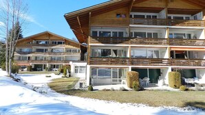 Un bâtiment en bois à plusieurs étages, doté de balcons, d’un espace extérieur couvert et d’un sol recouvert de neige.