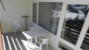 A balcony with a white table and chairs, a white chair, and a view of a snowy landscape through large windows. - La Sarine 222 by Interhome (Gstaad)