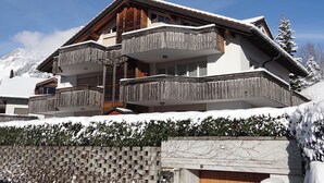 Una cabaña de varios pisos con un balcón de madera, con vista a una montaña nevada.