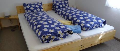 A double bed with a wooden frame, two pillows with a daisy pattern, and a blue blanket.