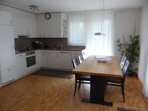 A modern kitchen with white cabinets, a wooden dining table, and a clock on the wall.