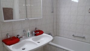 Un baño con lavamanos blanco, dos grifos, un espejo y una bañera.