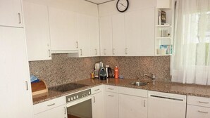Una cocina con armarios blancos, encimera de granito, cafetera, tostadora y un reloj en la pared.