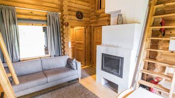 A log cabin interior with a gray sofa, a fireplace, and a wooden shelf with logs.