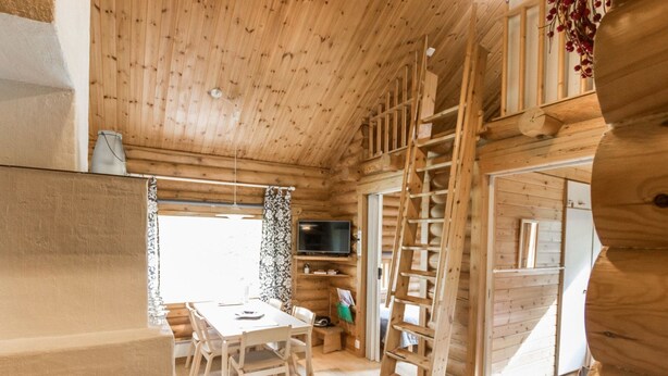 L’intérieur d’une cabane en bois comprend un coin repas, un téléviseur et une échelle.