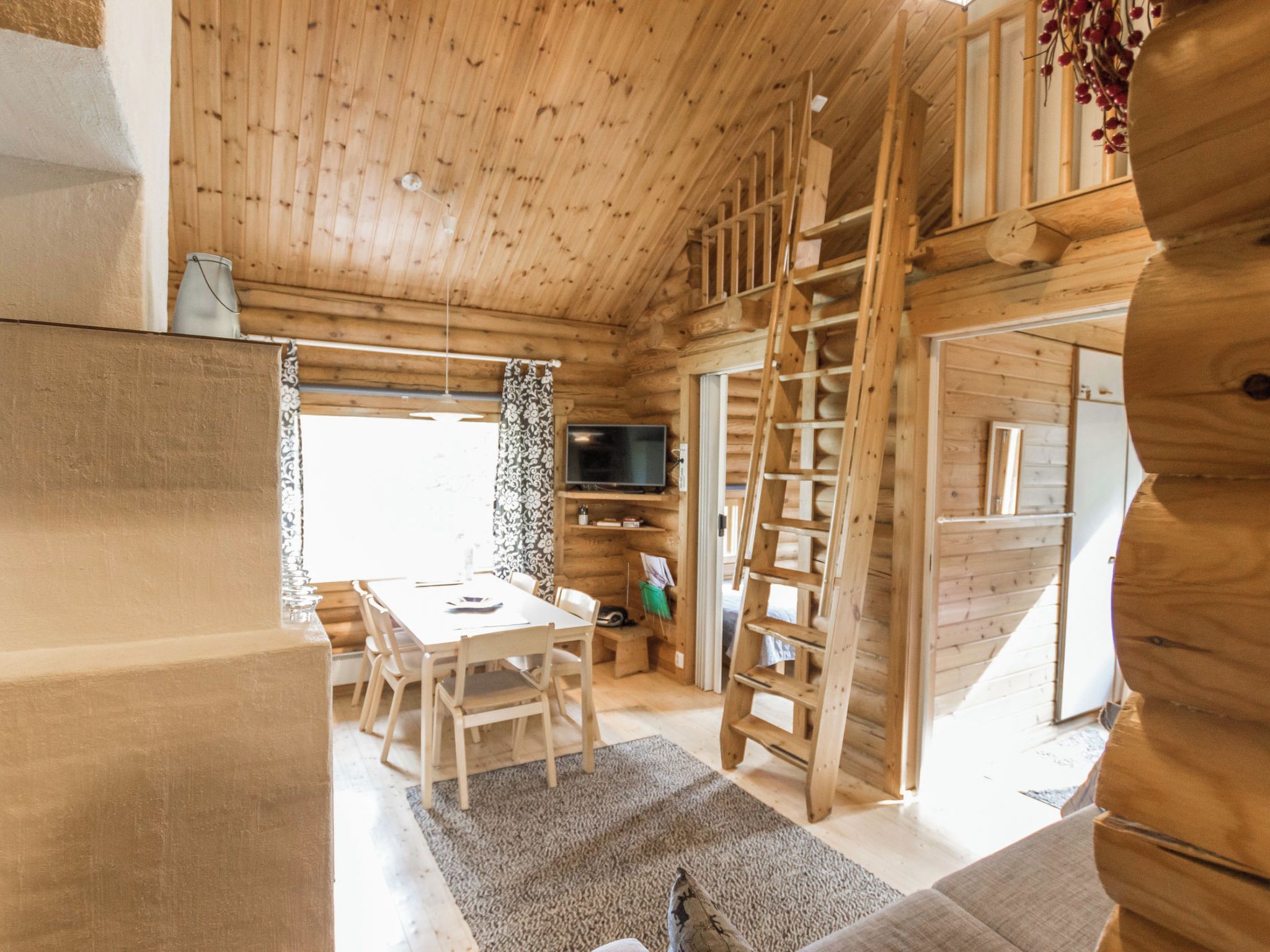 Interior de uma cabana de madeira com área de jantar, televisão e escada.