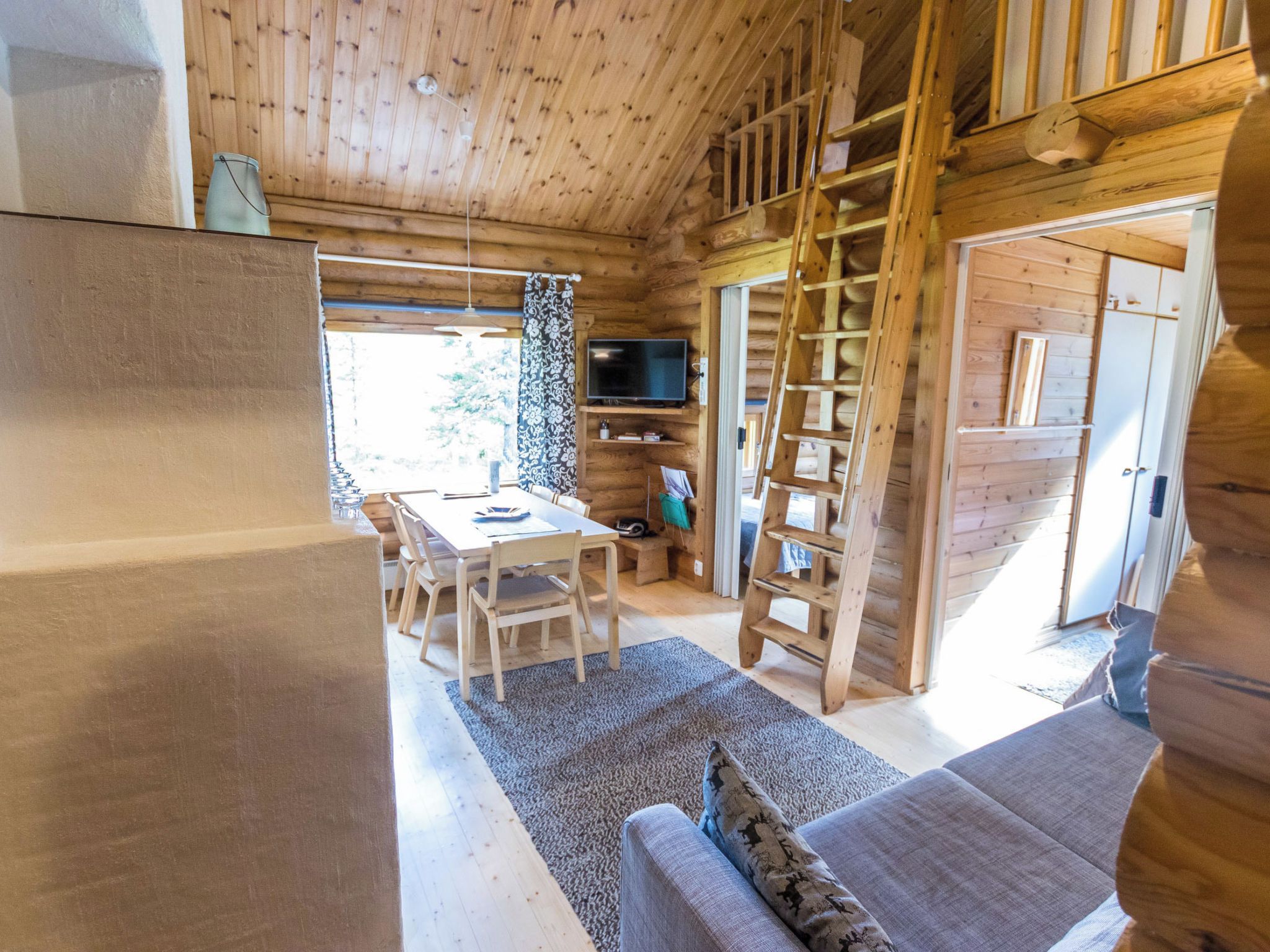 Interior de cabana de madeira com área de jantar, sofá, televisão e escada.