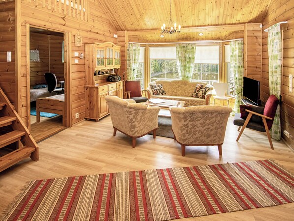 A wooden cabin interior with a sofa, chairs, a TV, a radio, and a staircase. - Polaria by Interhome (Forssa)