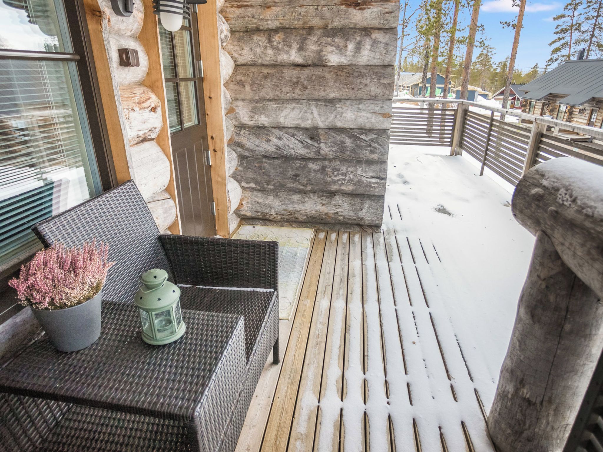 A wooden deck with a wicker table and chairs, a lantern, and a stone wall.