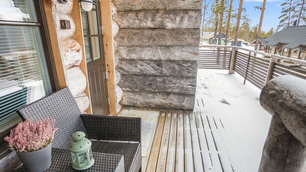 A log cabin with a balcony featuring wicker furniture, a potted plant, and a lantern. - Maahisenrinne 1 as 4 by Interhome (Äkäslompolo)