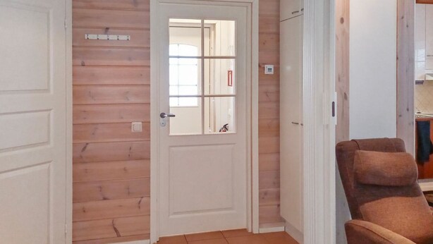 A room with wooden walls, a white door with a glass panel, and a brown armchair. - Hovitahko a 1 by Interhome (Nilsiä)