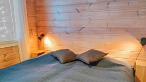 A wooden cabin room with a bed, two pillows, and a nightstand with a lamp. - Hovitahko a 1 by Interhome (Nilsiä)