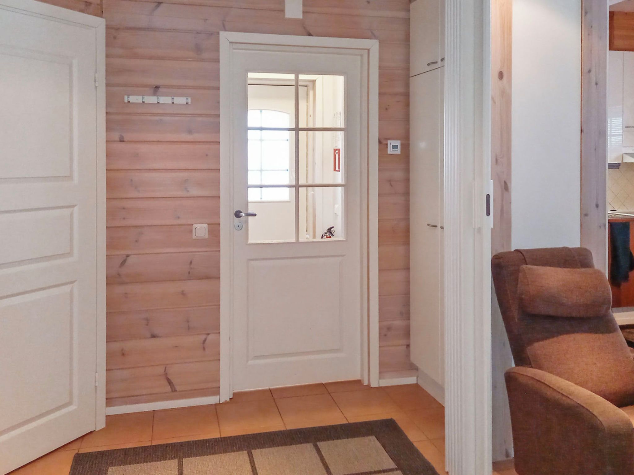 A wooden interior with a white door, a brown chair, and a tiled floor.
