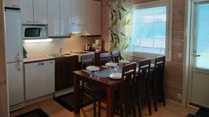 A compact kitchen with white cabinets, a microwave, and a coffee maker. There is a dining table with chairs and a window with blinds. - Hovitahko a 1 by Interhome (Nilsiä)