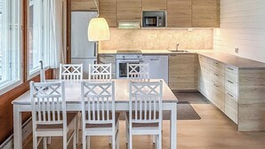 Et moderne køkken med træskabe, en central ø og et spiseområde med hvide stole.